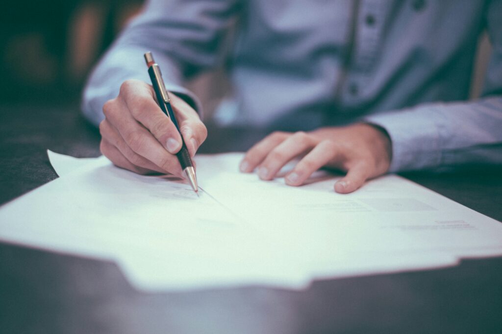 A close-up of a buyer signing a property sale and purchase contract next to a set of house keys and a fountain pen.