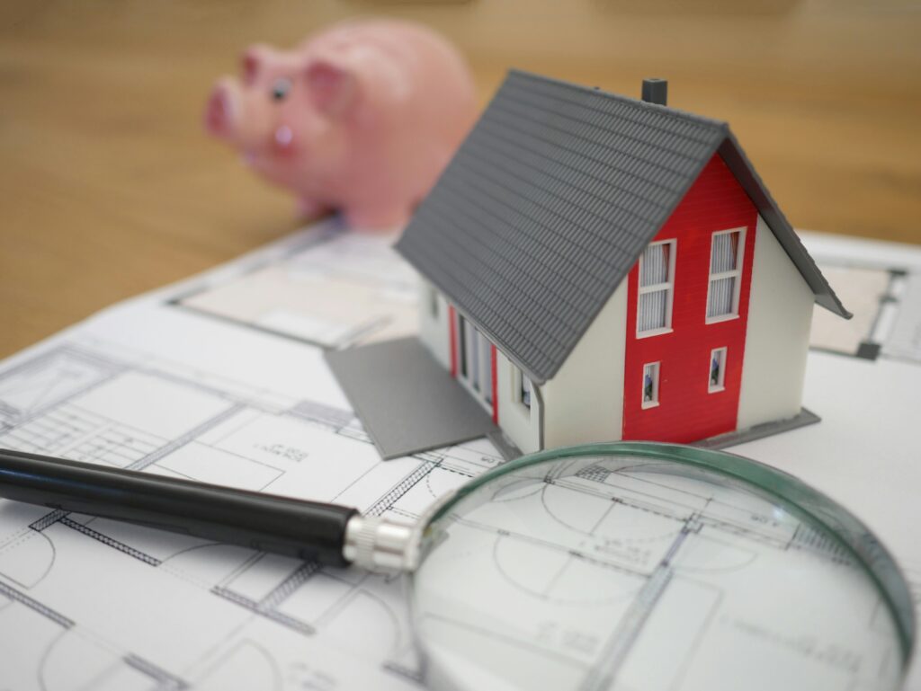 Close-up of a magnifying glass inspecting a house floor plan, representing the comparative market analysis and property shortlisting performed by a licensed agent.